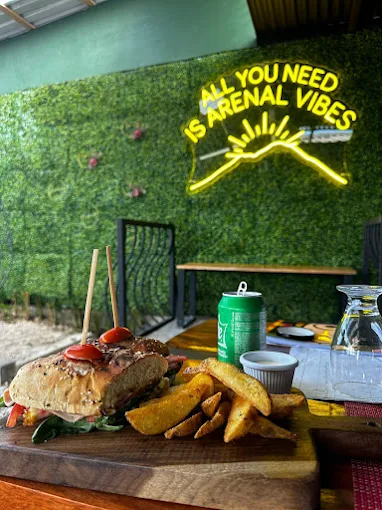 Signature Picnic burger with potato wedges in front of an 'All You Need Is Arenal Vibes' neon sign.