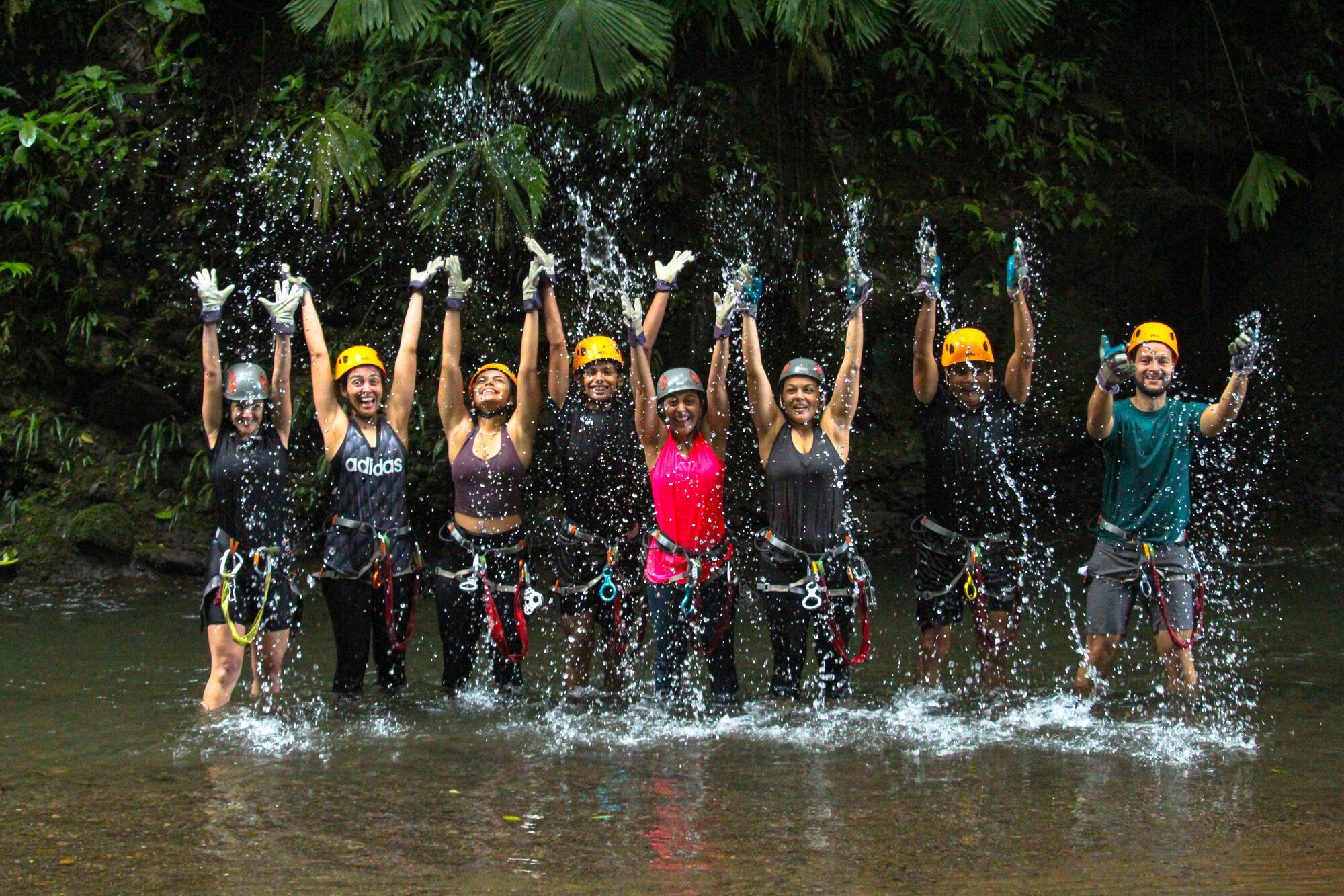 Group celebrates with raised hands under a rainforest waterfall splash.