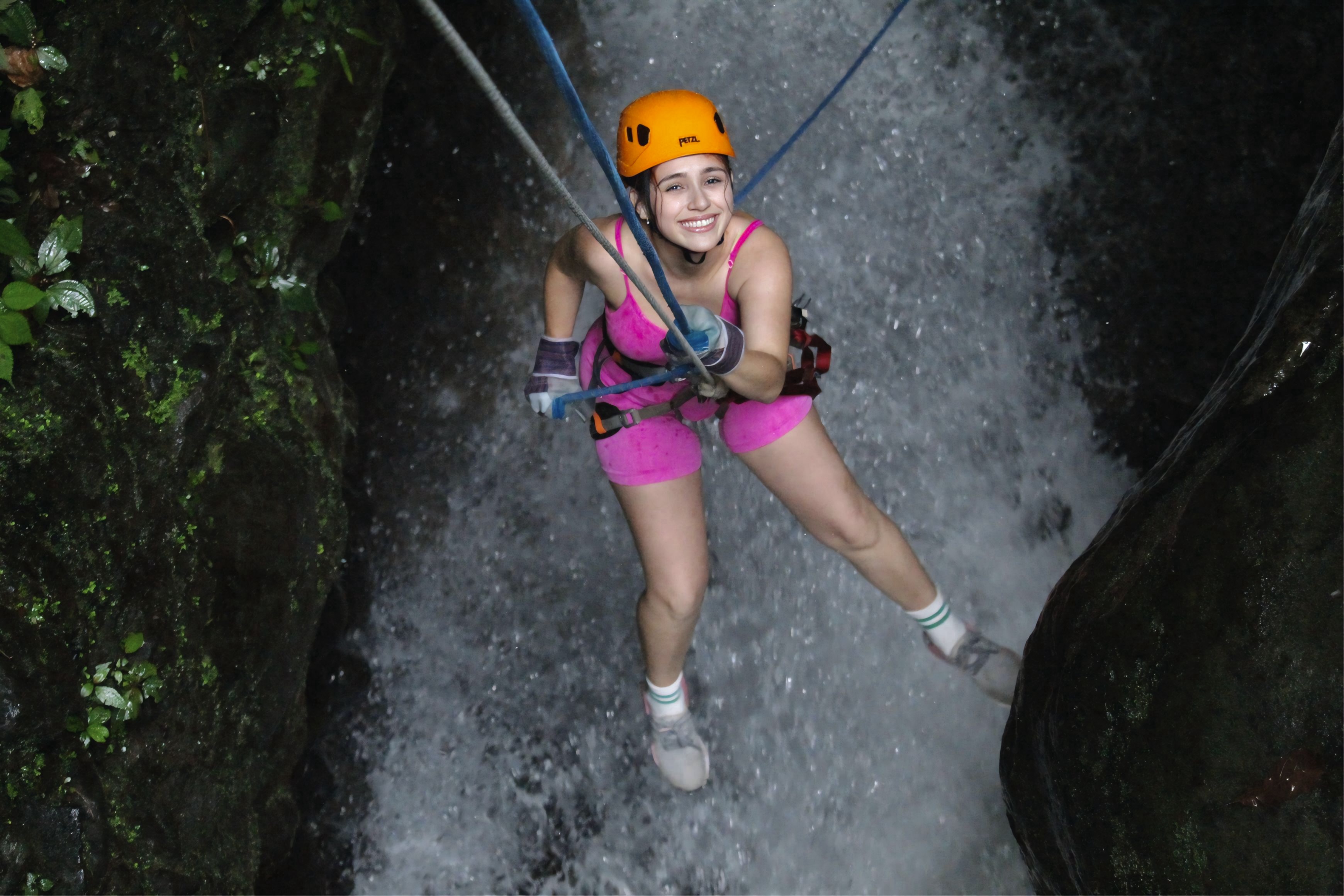 Guest rappels down a waterfall in pink gear, smiling at the camera.