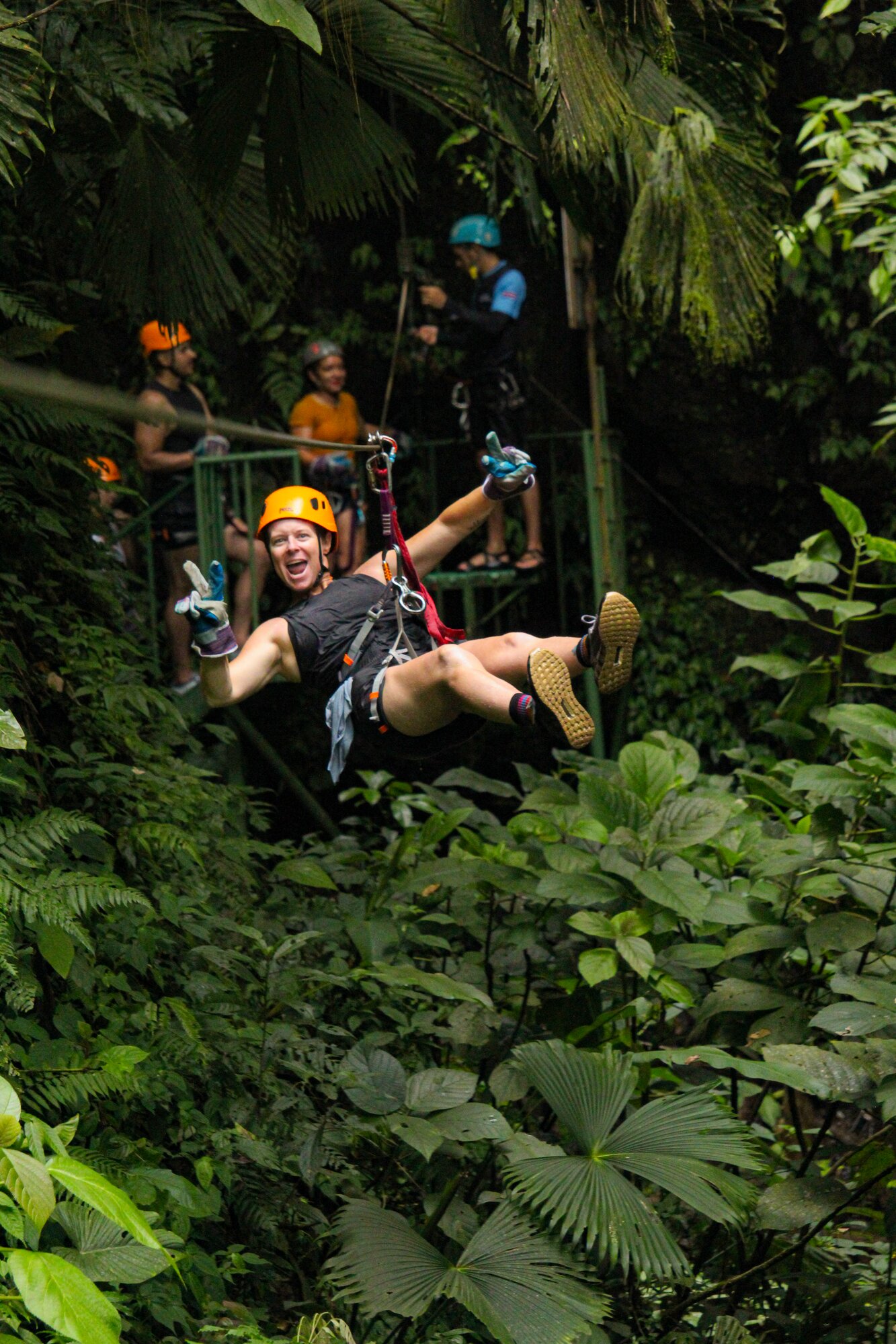 Zipline rider gliding through dense rainforest canopy.