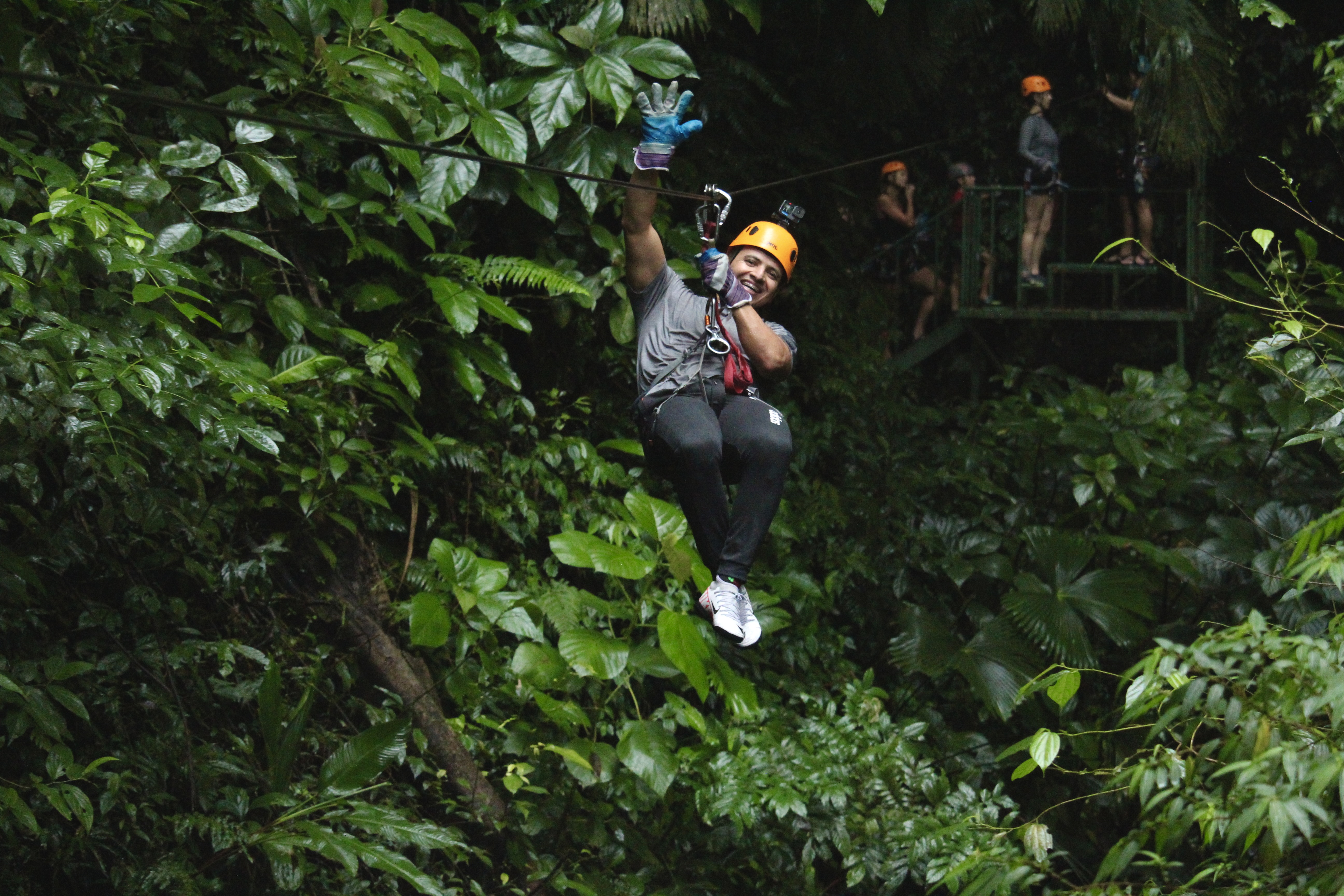 Guest ziplining through tropical greenery toward the camera.