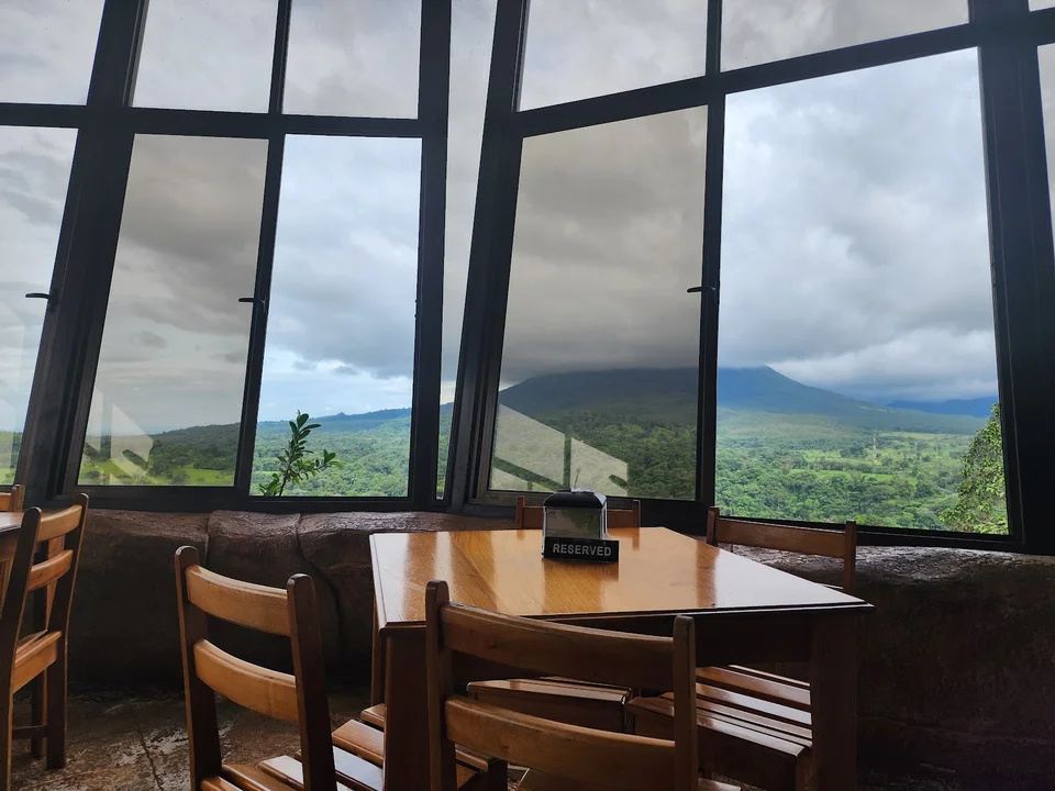 Dining room with floor-to-ceiling windows opening onto Arenal Volcano and rainforest.
