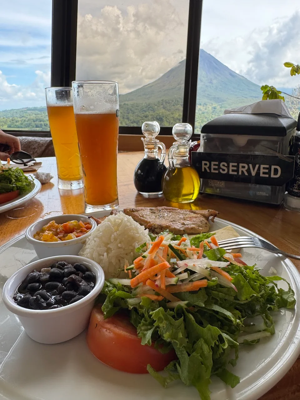 Costa Rican casado plate with beer and Arenal Volcano framed in the window behind.